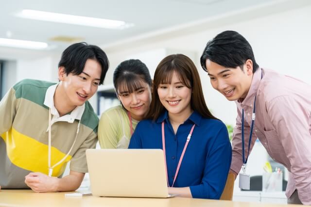 ノートパソコンを見て微笑む四人の同僚