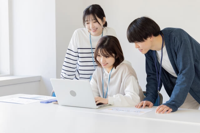 パソコンで協力して作業する三人